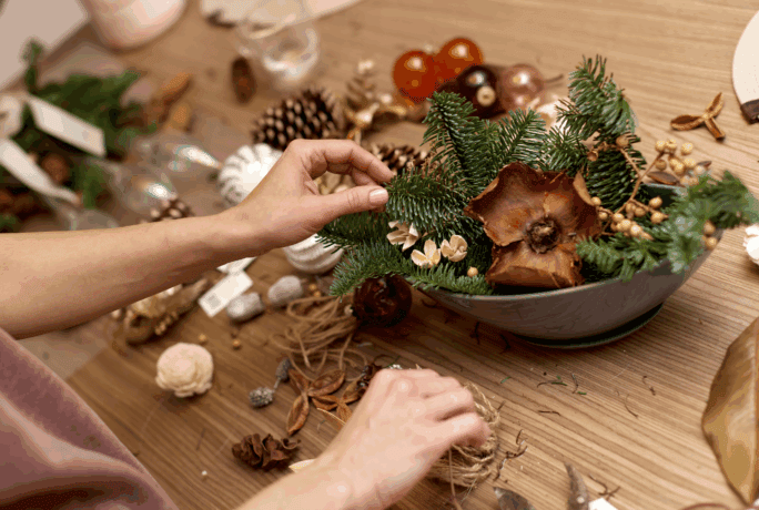 Een bovenaanzicht van handen die een kerststukje maken